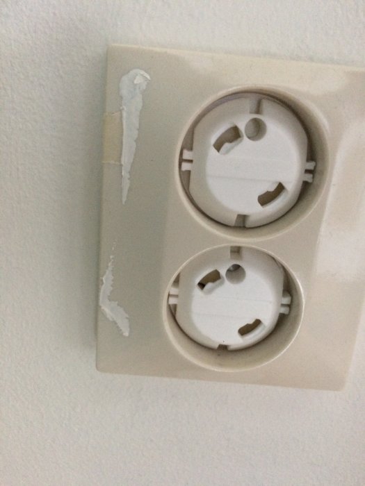 Ett vägguttag med installerade petskydd och märken efter borttagen färg på den omgivande väggen.