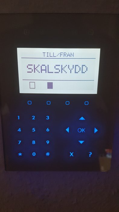 Larmpanel visar skärmen med texten 'TILL/FRÅN SKALSKYDD' och valknappar lyser blått.