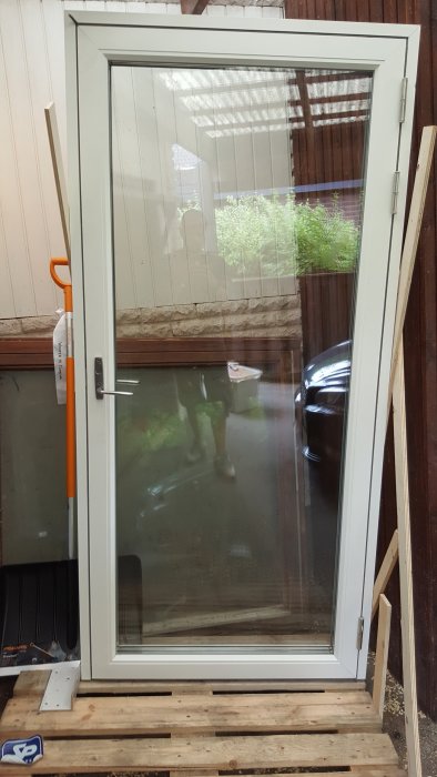 Vit trä- och aluminiumfönsterdörr med högerhängning står på en pall, med repor synliga och rester av mjukfog på karmen.