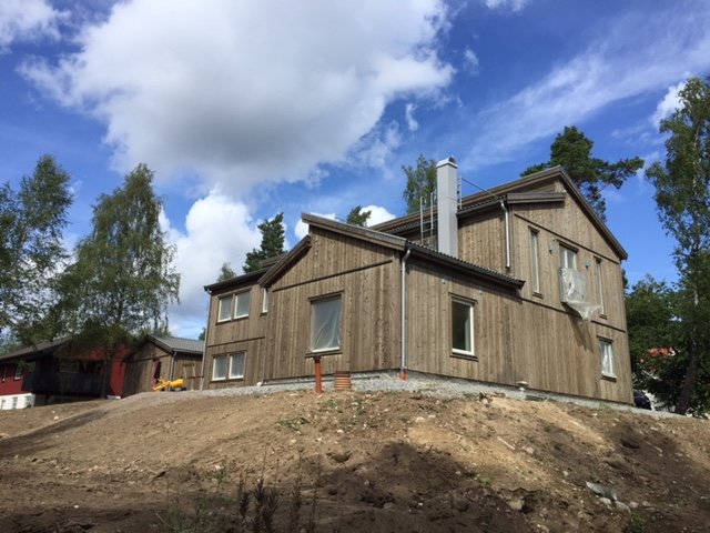 Nyligen behandlat trähus och carport i brungrå nyans med skyddstejp på fönster.