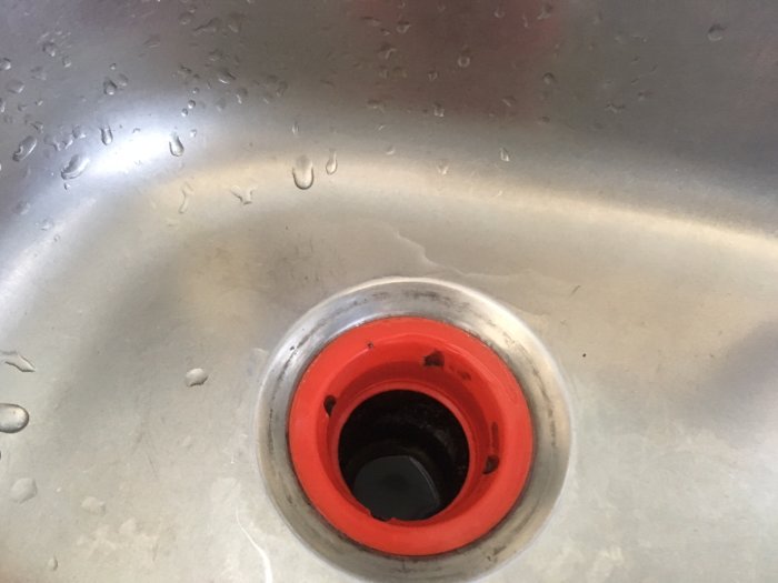 Närbild på ett vattenlås i diskho med en röd plastdel som har fyra urgröpningar inuti.