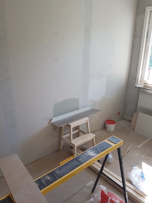 Renoveringsrum med nymålade väggar i ljus "Lammull", färgprover mot golv och golvsockel, oavslutad renovering.