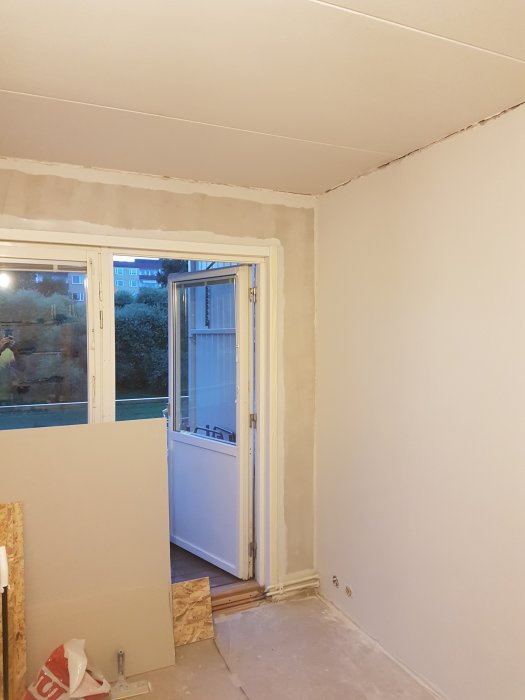 Renoveringsprojekt med nymålade väggar i nyansen "Lammull", gipsskarvar synliga, vid öppen balkongdörr.