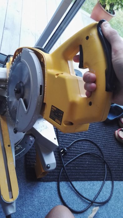 Gul gersåg med svart handtag hålls nära fönster, inställd på 45 graders vinkel med synlig sågklinga.