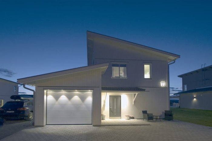 Extern belysning på ett hus i skymning med nedåtriktade spotar över garageport och entré.