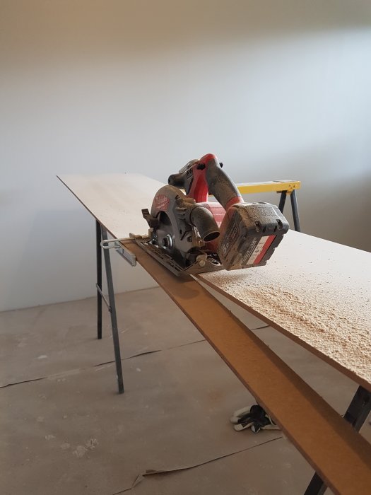 En cirkelsåg på en arbetsbänk med nysågad bräda och spån på golvet under renovering.