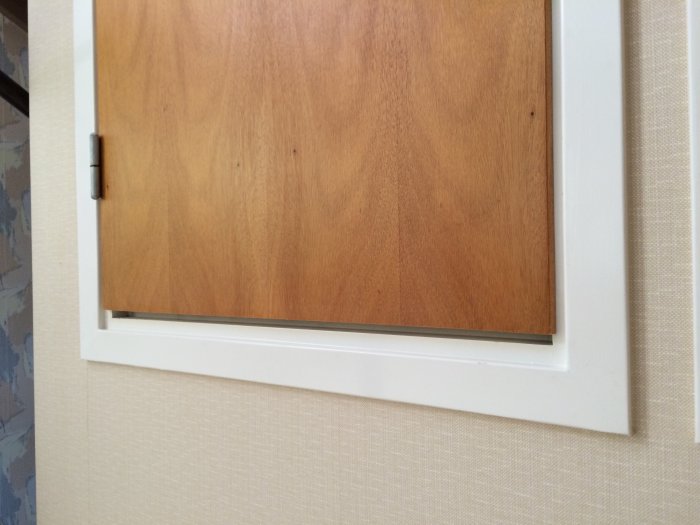 Närbild av en nyligen monterad träskiva i en vit dörrkarm mot en tapetserad vägg.