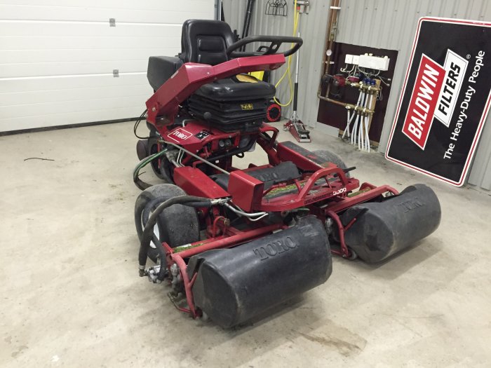 Röd Toro Greensmaster 3000 gräsklippare i ett garage som behöver nya däck och service.