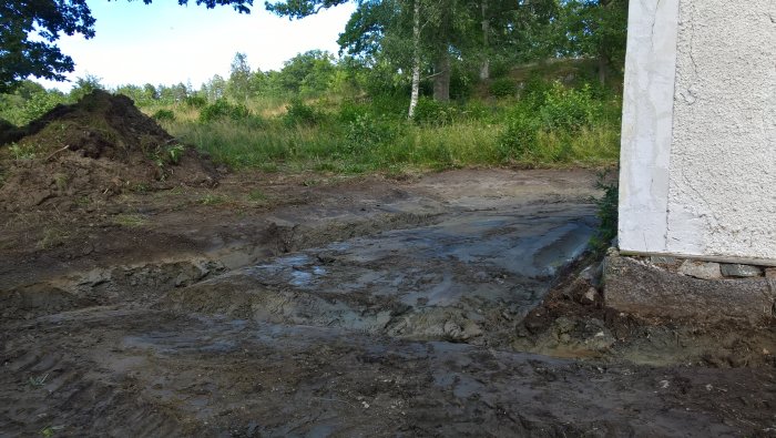 Renoveringsområde med schaktad lera och ny dränering vid vit byggnad.