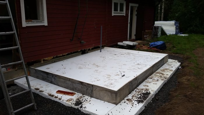 Förberedd betongplatta redo för gjutning av grund till farstukvist vid röd husvägg.