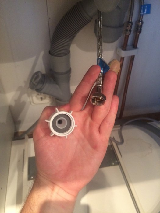 Hand håller vattenanslutningar med olika diameter framför synliga rör och slangar.