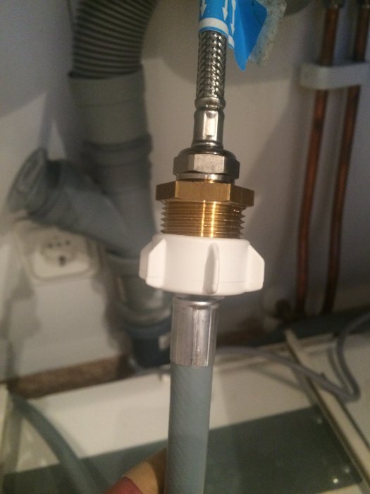 Närbild av en hand som håller en vattenledningsnippel med ansluten vattenslang och blandare i ett kök.