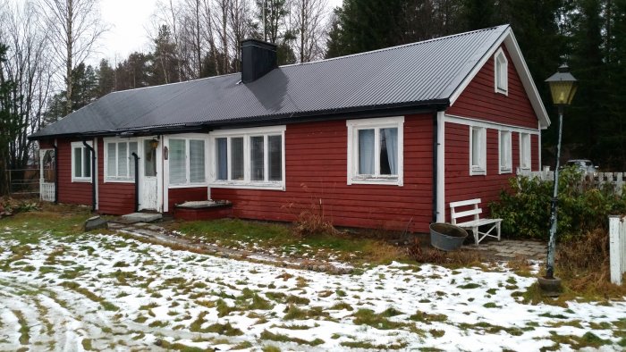 Rött trähus med snöfläckar på gräset och en överbyggd låda som är genomrutten.