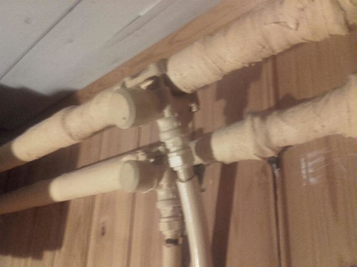 Isolerade rör och ventiler som kopplar till ett element i ett källarutrymme.