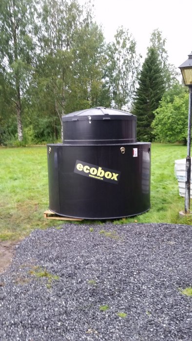 Ett nytt avloppsreningsverk märkt "ecobox" står på grus med grönskande träd i bakgrunden.
