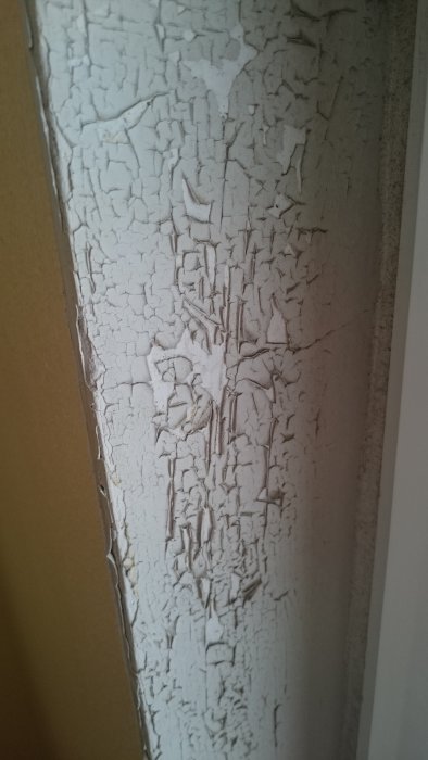 Avflassende hvit maling på vegg, med sprekker og flass som viser behov for restaurering og vedlikehold.