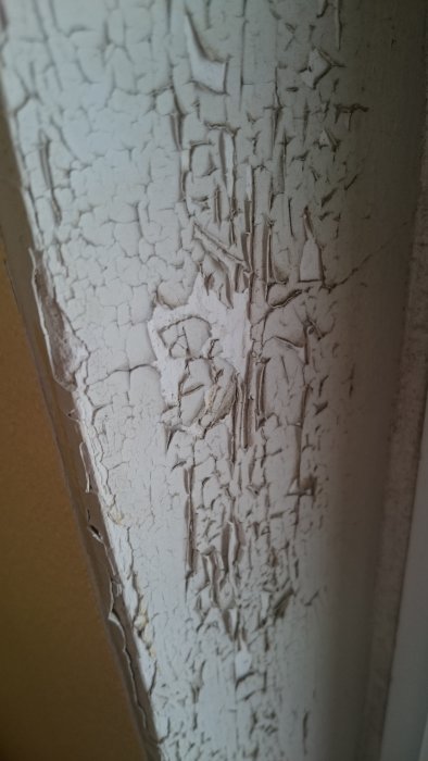 Avflassende hvit maling på slitt dørkarm med synlige sprekker og flater som trenger renovering.