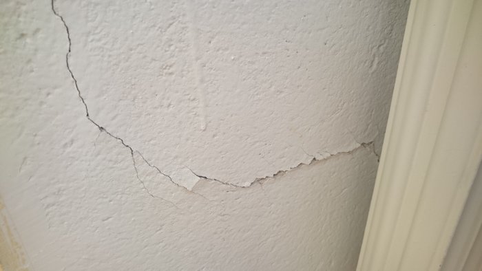 En vegg med avflassende maling og synlige sprekker nær en dørkarmlist.