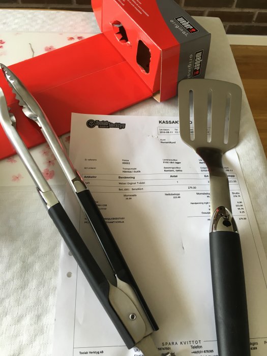 Grilltång och stekspade från Weber på kvitto med Toolabs logotyp, förpackningar i bakgrunden.