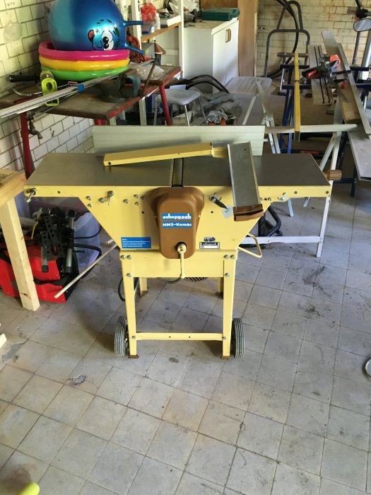 En rikt/plan hyvel av märket Scheppach i ett verkstadsutrymme med diverse verktyg och byggmaterial i bakgrunden.