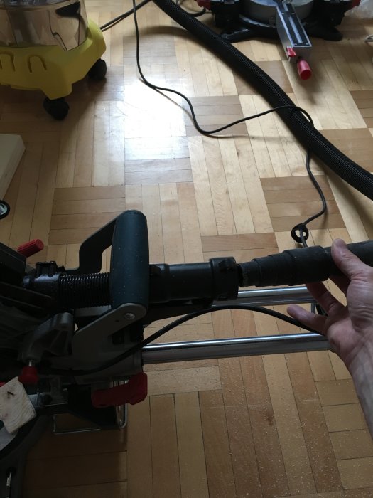 Hand håller en Kärcher-adapter ansluten till verktyg, med golv och städutrustning i bakgrunden.