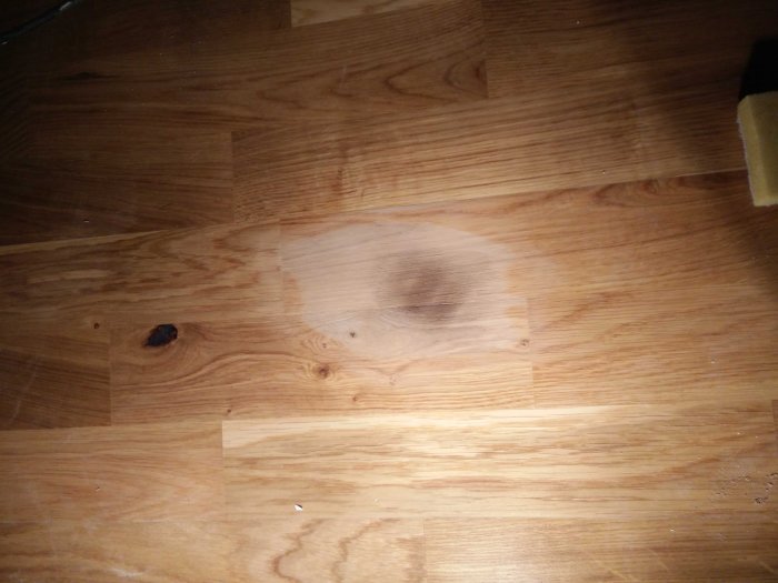 Parkettgolv med en mörk, ytligt bränd fläck orsakad av en välta bygglampa.