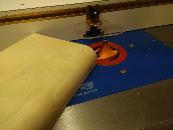 En träbit nära en frässpets på ett anpassat blått fräsbord kopplat till en Bosch GTS 10XC bordssåg.