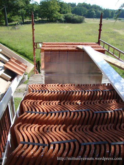 Takpannor staplade på varandra på en byggställning med grönt fält i bakgrunden.