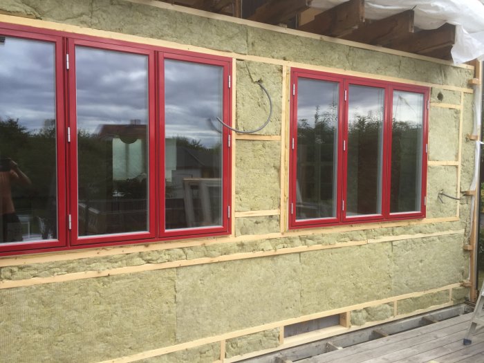 Nyisolera husvägg med vindduk och Röda fönsterramar under renovering.