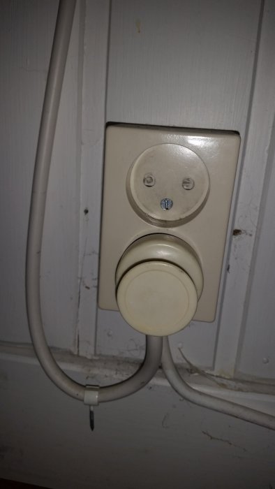 Ej jordat vägguttag med inkopplad kabel för utomhuslampa på en vit vägg.