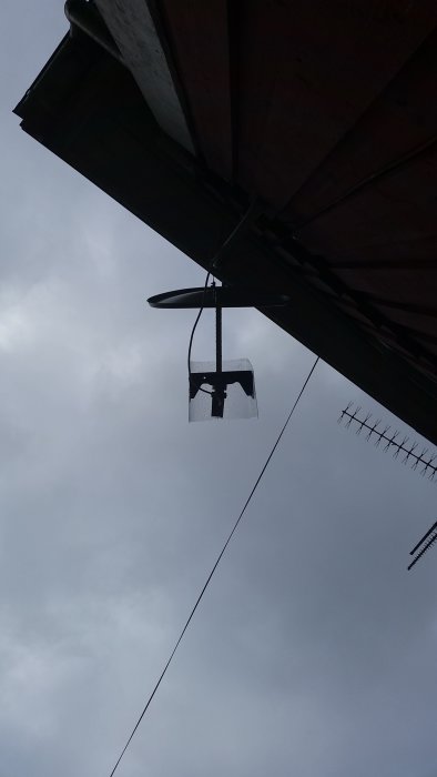 Vy underifrån på en Viasat-parabol monterad på en huskant med vinklat LNB-huvud mot en molnig himmel.