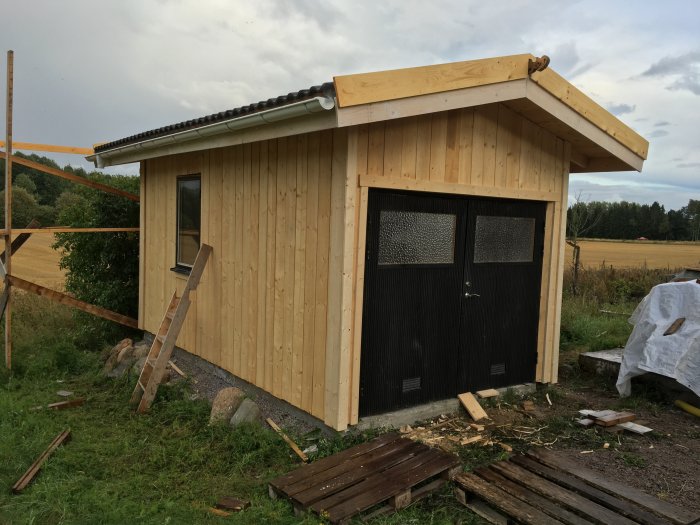 Nyinstallerade svarta dubbeldörrar på en obehandlad träfasad på ett litet byggnadsprojekt.