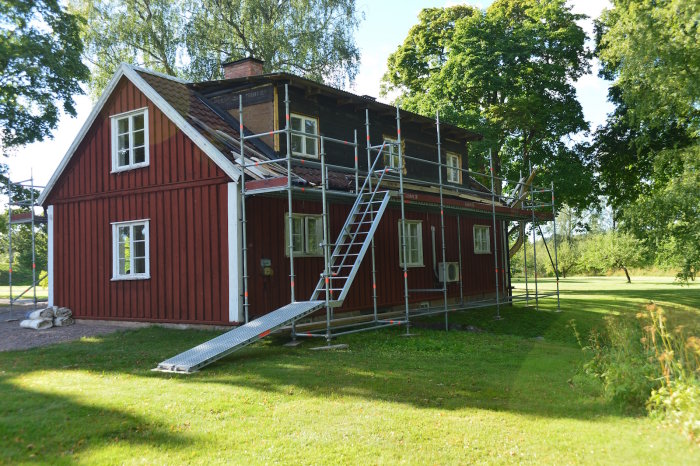 Rödmålad stuga med pågående renovering och uppställda byggställningar runtom.