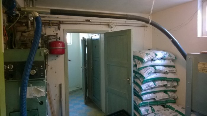 Ett pannrum med värmesystem, öppen dörr och en trave med vita säckar av isoleringsmaterial.