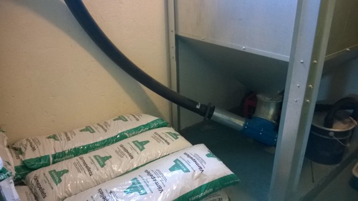 Förrådsutrymme med isoleringsmaterial och ett stort svart rör genom rummet.