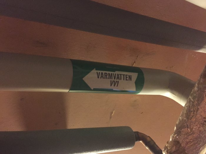 Värmesystemrör markerat med "VARMVATTEN VV1" under en träbjälke.