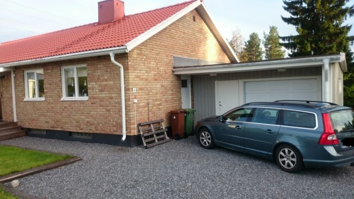 Ett enfamiljshus med tegelfasad och rött tak visar garage och entrédörr i behov av färgval.