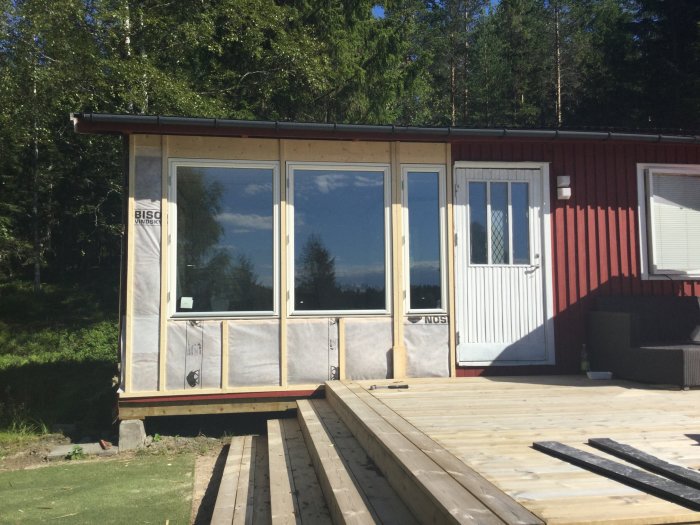 Nyinstallerade fönster och vindspärr på en fasad av ett hus med synlig isolering och en träterrass i förgrunden.