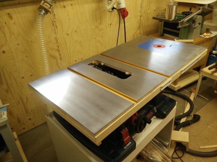 Anpassade ståltoppskivor på ett hemmabyggt bord för en bordssåg i en verkstad.