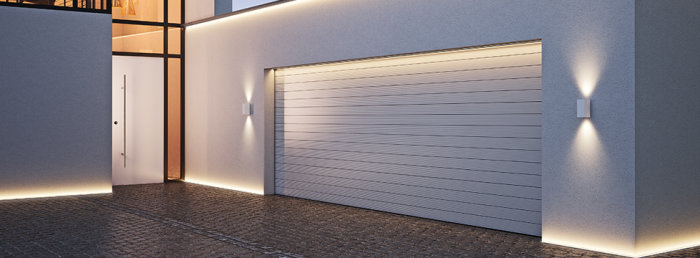 Modern husfasad med LED-listbelysning vid marken och vägglampor som ger diffus belysning vid garageporten.