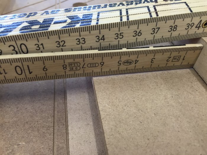 Tumstock placerad på en ände av en Björkplywoodskiva för att mäta tjockleken.