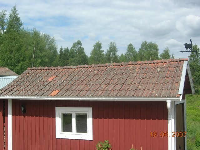 Gammalt tegeltak med mossa och smuts på ett rött hus med vit knut och fönster, behandlat med bensaltensid.