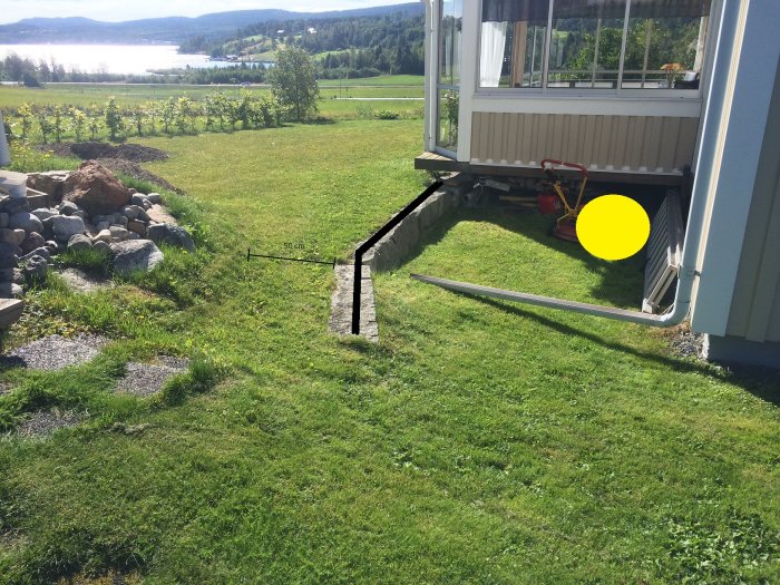 Trädgård med gräs, stenmur och handjagare under altan, gul markering där laddstation kan placeras.