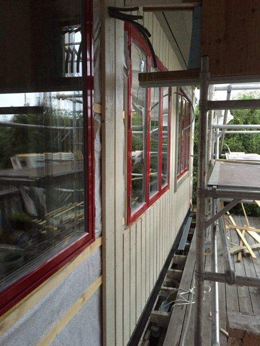 Renoveringsarbete på balkong med nya fönster, dörr och isolerade väggar med byggnadsställning.