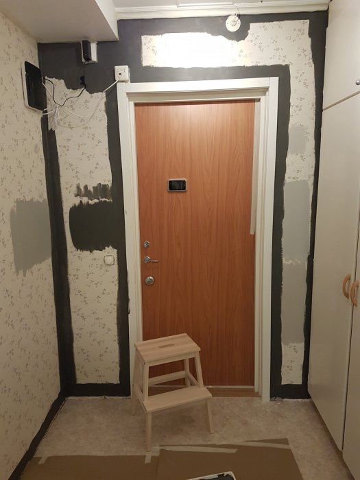 En hall under renovering med väggar delvis målade i en svartbrun nyans, omålad dörr, och en stege.