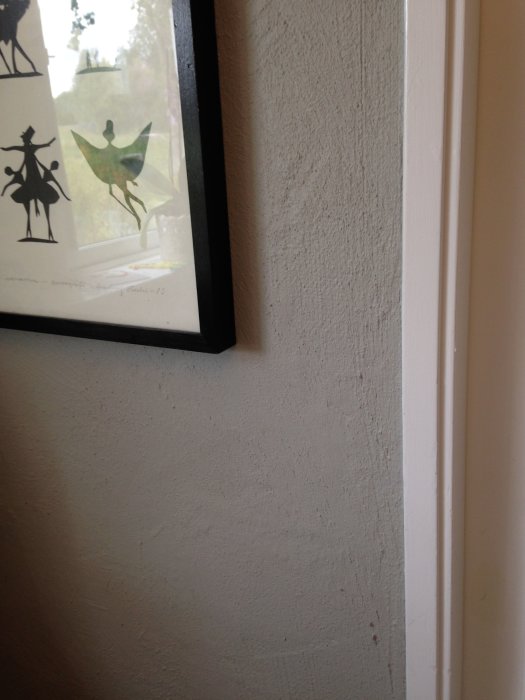 Kraftig strukturerad vitmålad vägg med synliga ojämnheter och vit dörrkarm, konstverk syns delvis.