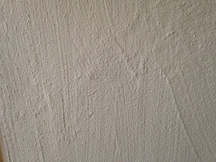 Vägg med grov struktur och ojämnt pålagd målning som ser hemmagjord ut.