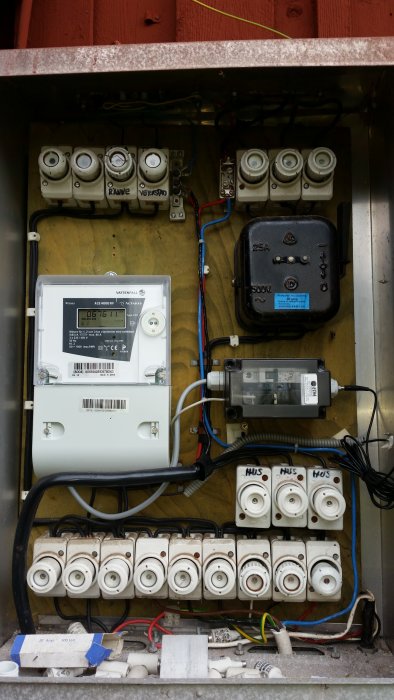Elektrisk huvudcentral med gammal utrustning, elmätare, säkringar och kablar i en fördelningsskåp.