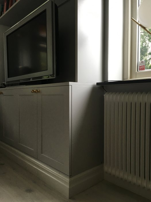 Närbild av grå bokhylla intill ett fönster och ovanför en vit radiator.