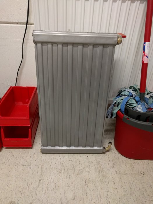 Nyligen blästrad radiator redo för nya fästen, med verktyg och redskapslådor i bakgrunden.